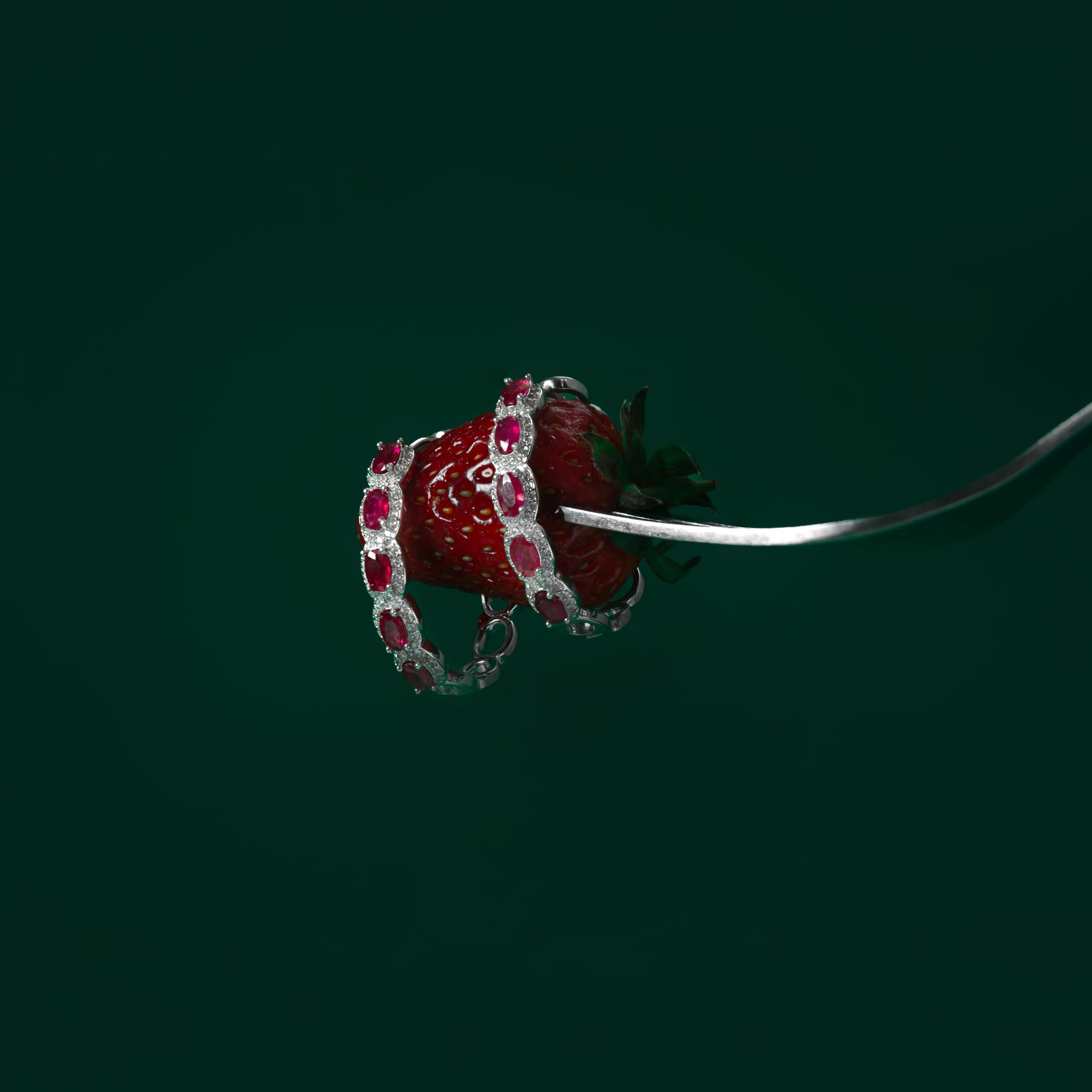 Earring 1c Strawberry wrapped in a jeweled silver bracelet with red stones against a dark green background.