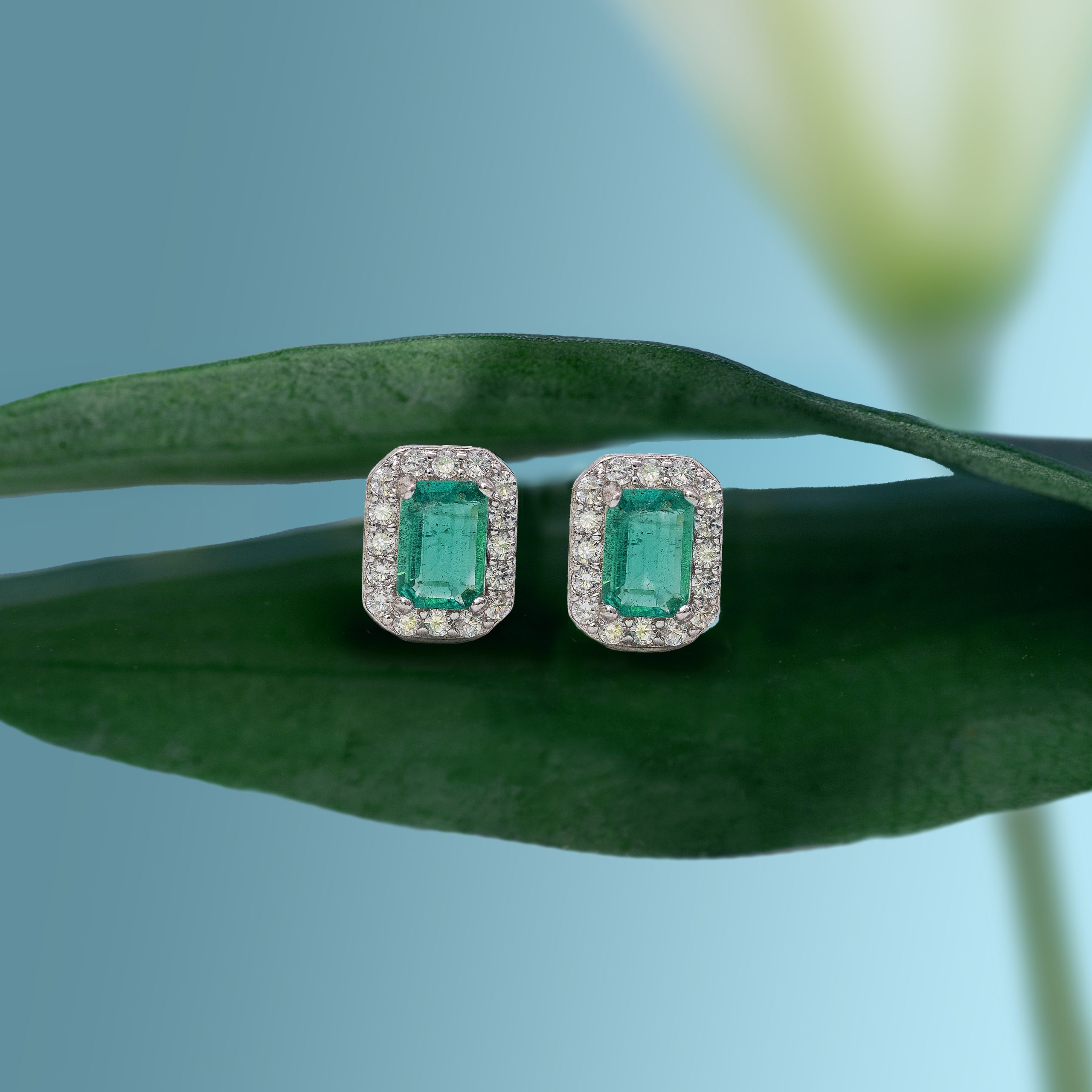 _NZR9533b Close-up of two emerald-cut emerald and diamond rings on green velvet display.