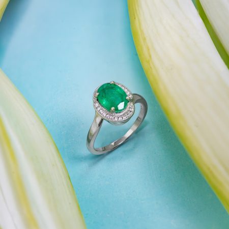 Close-up of a silver ring with a large emerald-cut green gemstone on a turquoise surface.