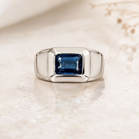 Silver ring with a square-cut blue gemstone in a polished bezel setting on a pale surface.