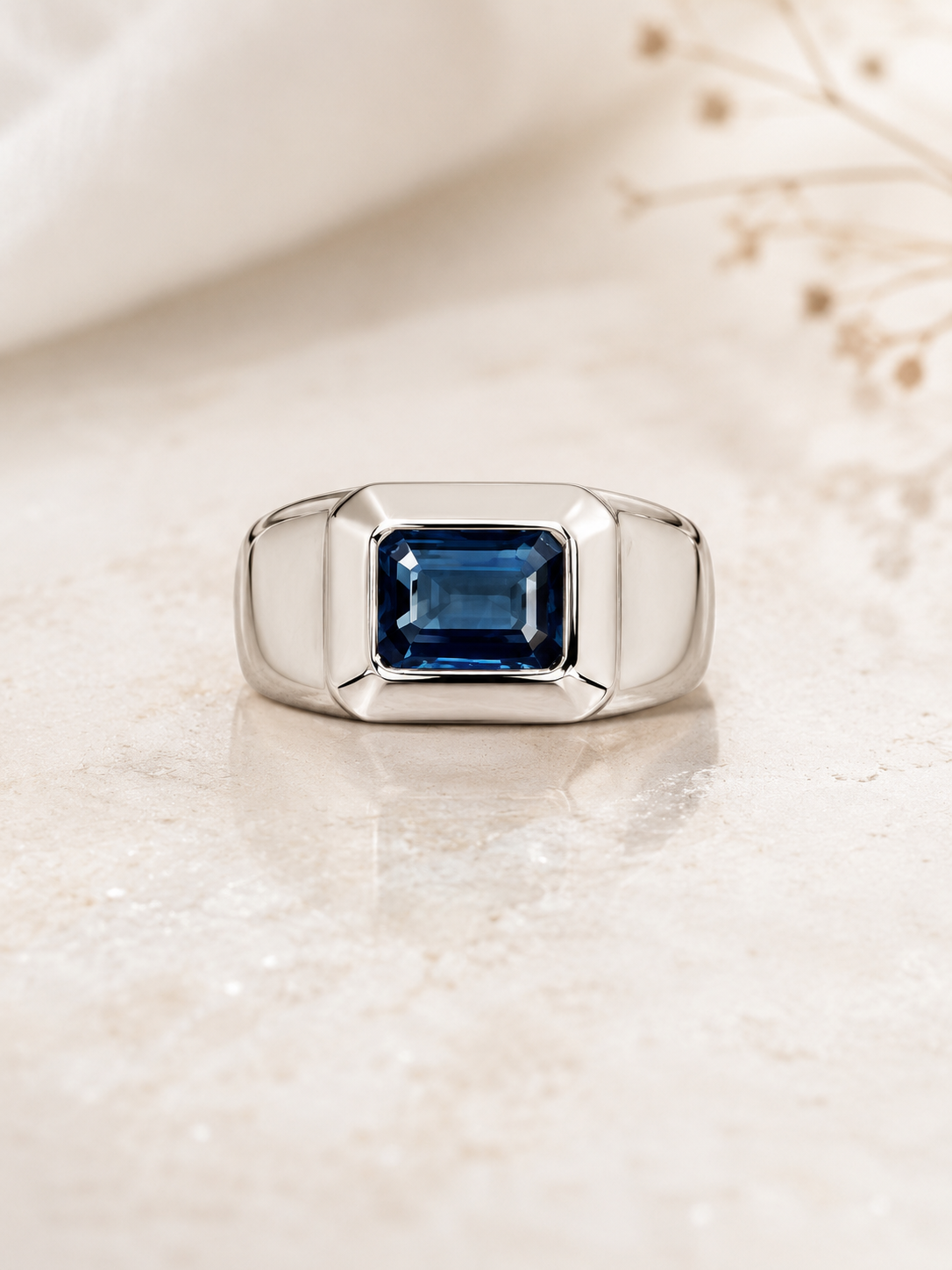 Blue-Sapphire-Ring-5 Silver ring with a square-cut blue gemstone in a polished bezel setting on a pale surface.