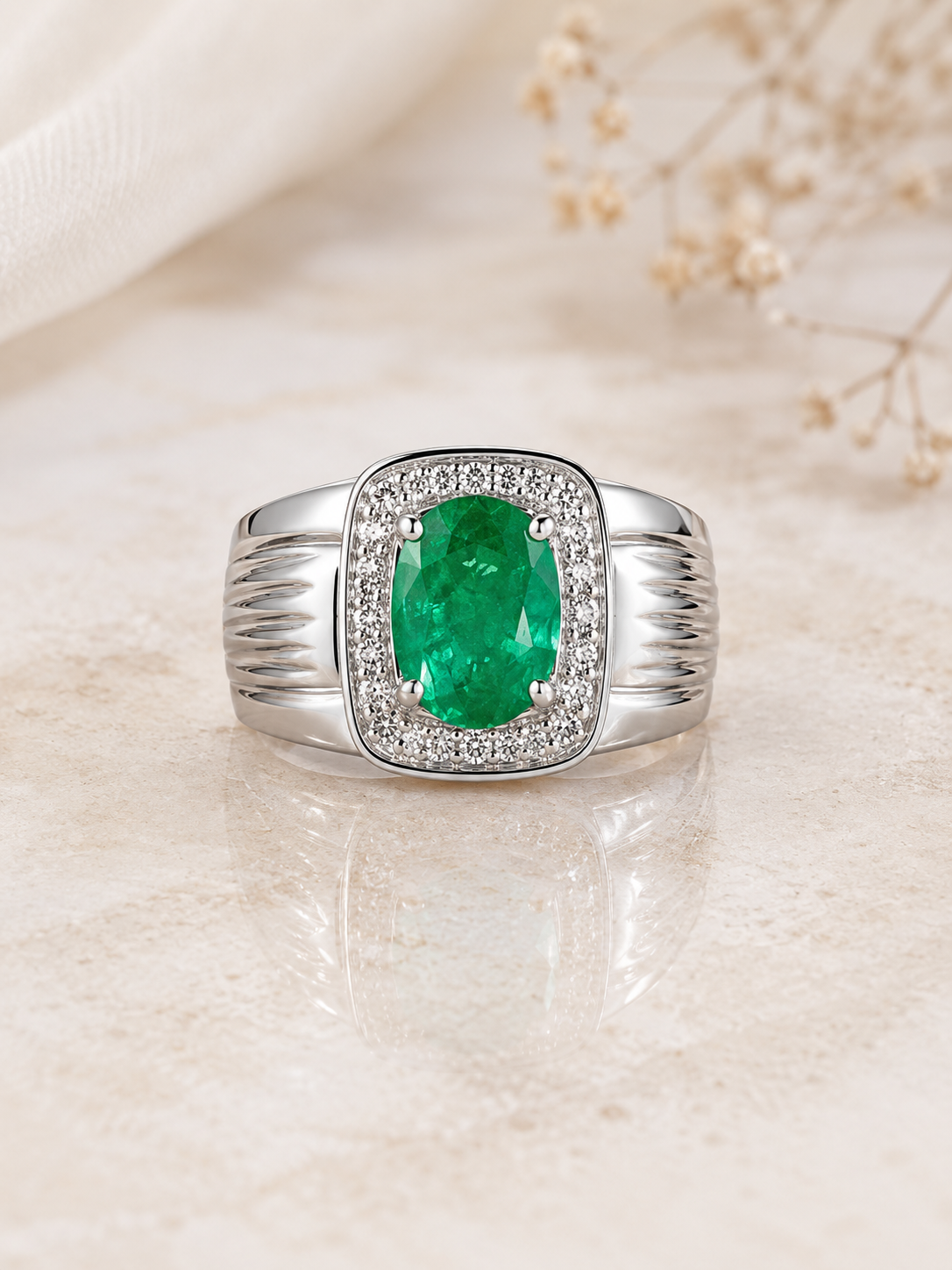 Emerald-Ring-3 Silver ring with an oval emerald center surrounded by a halo of diamonds on a beige surface.