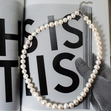 Pearl necklace laid over an open magazine with large black letters and a gloved hand touching the page.