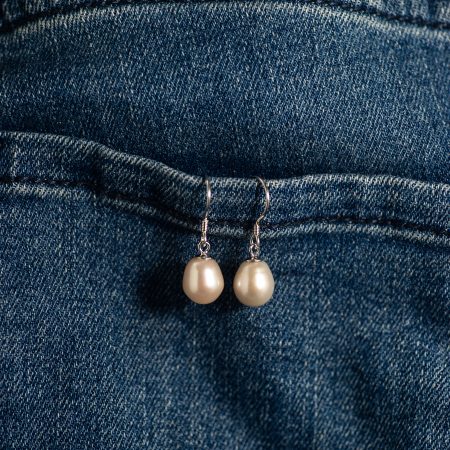 Pearl drop earrings hanging from the edge of a blue denim pocket on jeans
