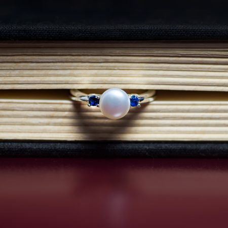 Close-up of a pearl ring with blue gemstones resting on a wooden surface.