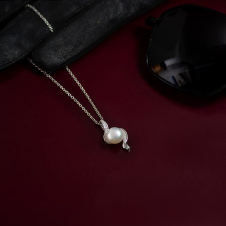 Pearl pendant necklace with a silver setting resting on dark red velvet, near a black jewelry case and black sunglasses.