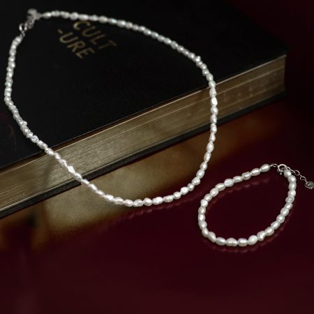 Pearl necklace draped over a dark hardcover book with gold-edged pages on a burgundy surface.