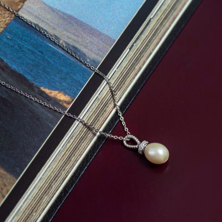 Close-up of a silver chain necklace with a pearl pendant resting along the edge of a glossy magazine page on a dark burgundy surface