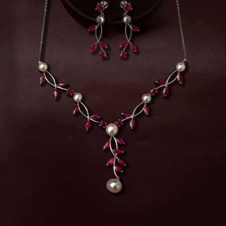 Jewelry set with a silver necklace featuring red gemstones and white pearls on a dark burgundy background