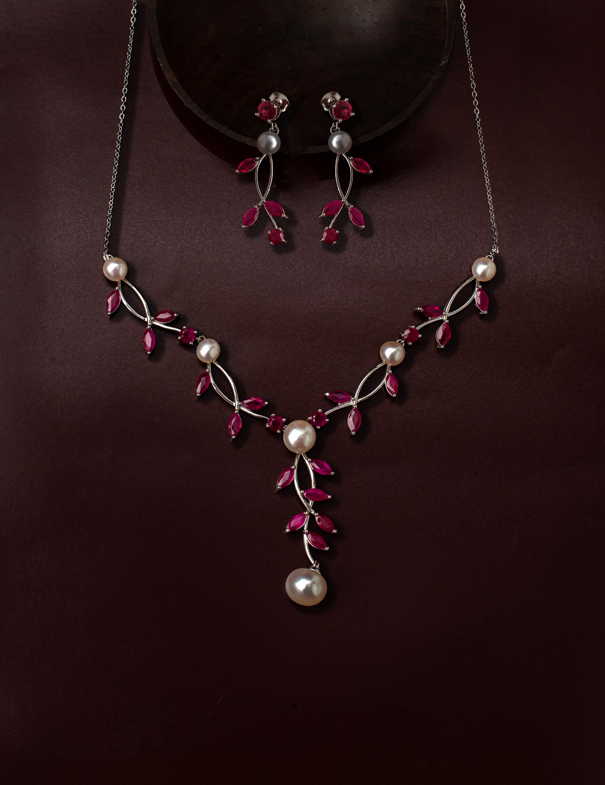 _NZR2182 Jewelry set with a silver necklace featuring red gemstones and white pearls on a dark burgundy background