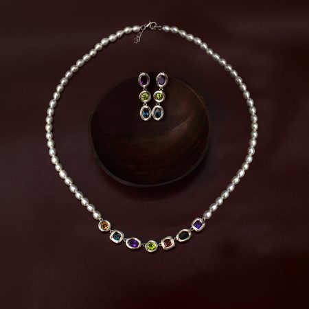Pearl necklace with matching three-stone drop earrings featuring purple, green, and blue gems on a dark burgundy background