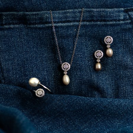 Pearl drop earrings and matching diamond-studded necklace laid on dark blue denim fabric near a pocket seam.