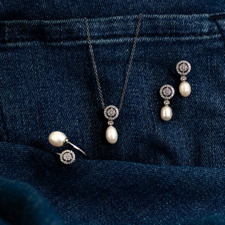 Pearl pendant necklace with diamond halo and matching drop earrings on dark denim backdrop