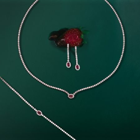 Diamond necklace with ruby-red teardrop pendants displayed on green background in a jewelry layout of loops and stones on emerald backdrop to highlight gems.