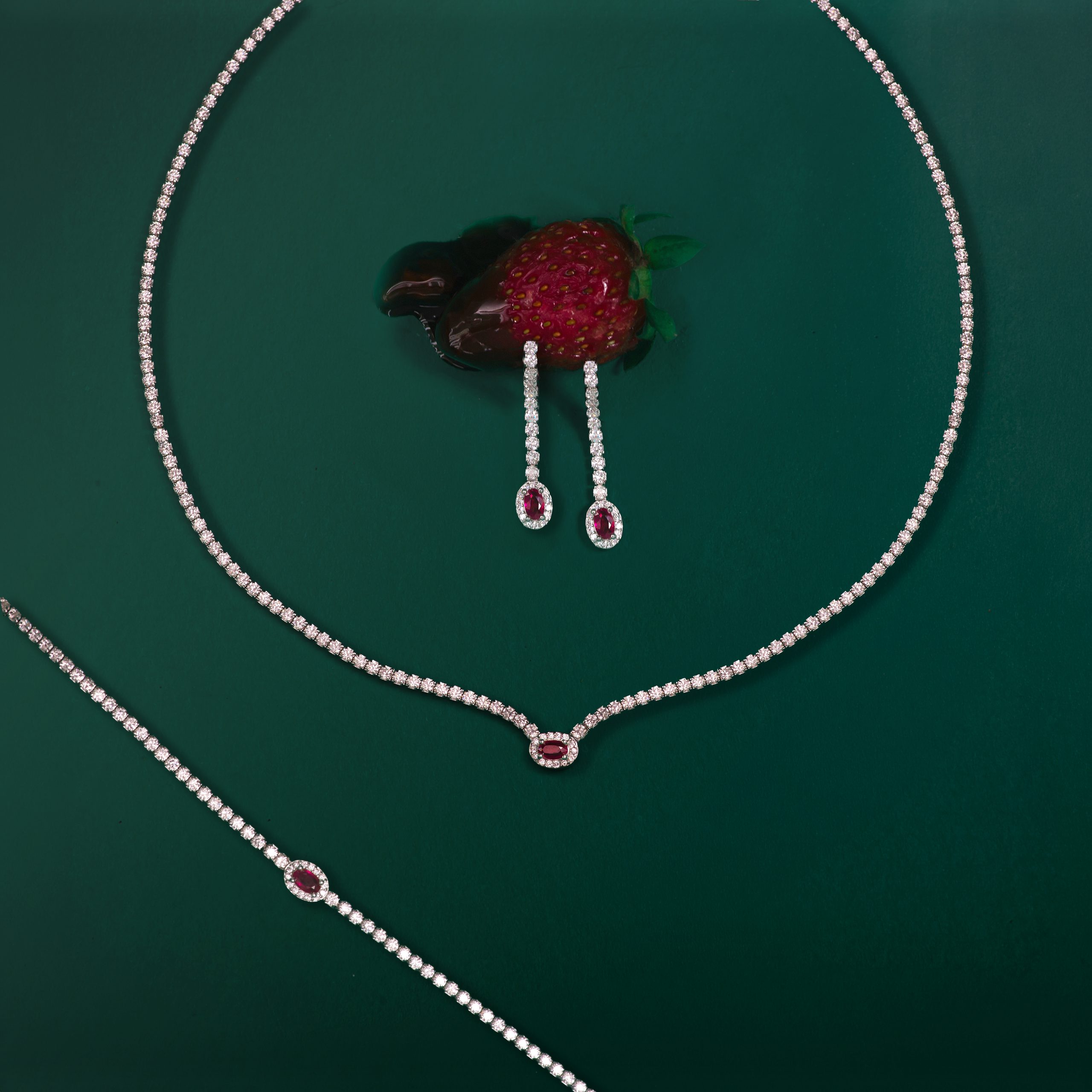 _NZR0026 Diamond necklace with ruby-red teardrop pendants displayed on green background in a jewelry layout of loops and stones on emerald backdrop to highlight gems.