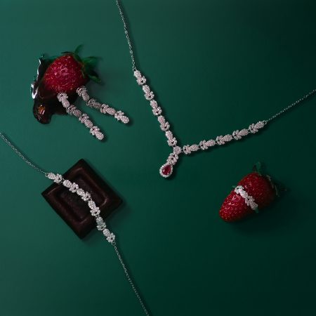 Diamond necklace laid on a green background beside strawberries.