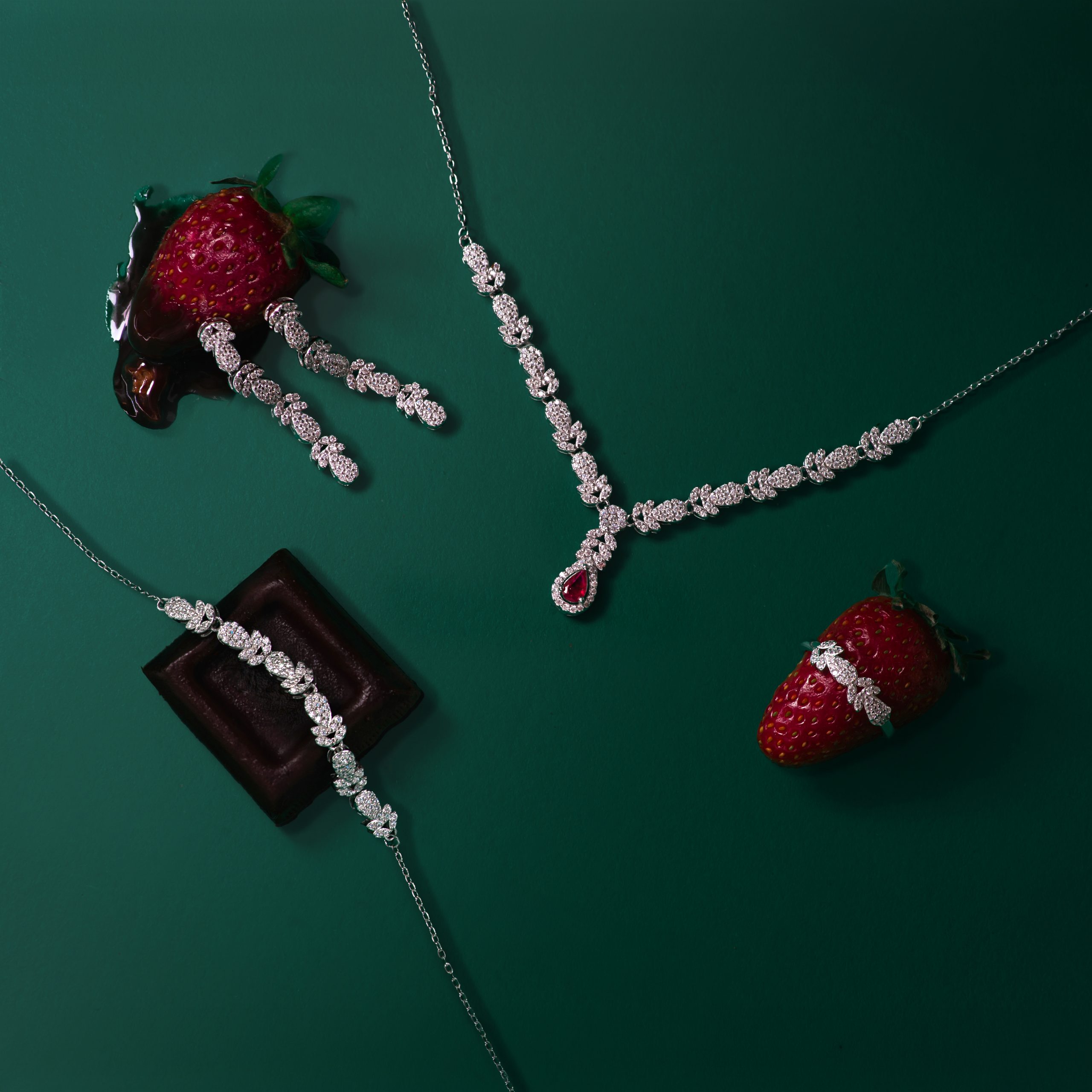 _NZR0083 Diamond necklace laid on a green background beside strawberries.