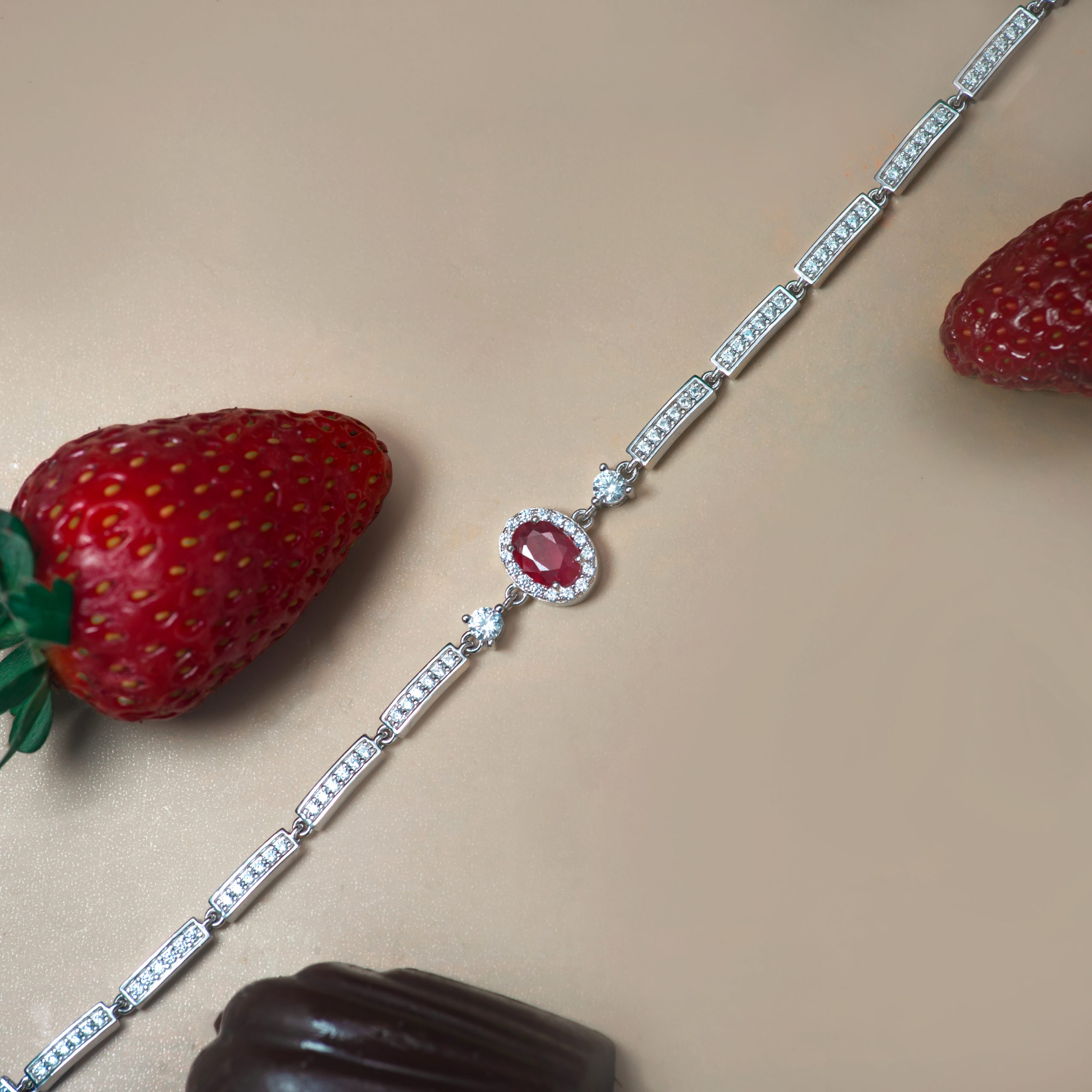_NZR9919 Diamond-encrusted bracelet with rectangular links diagonally placed on a beige surface, strawberries visible at the edges.