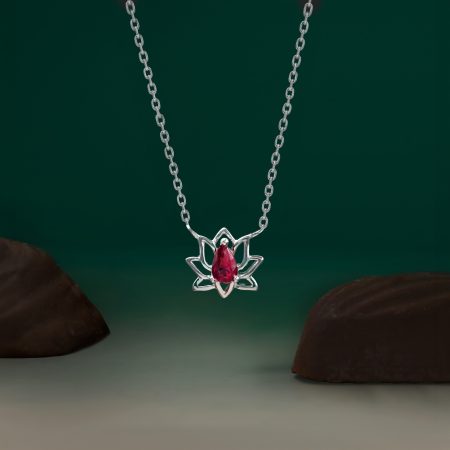 Silver necklace with a lotus-style pendant featuring a red gemstone, hanging against a dark green background.