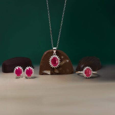 Silver chain necklaces with pink gemstone pendants displayed on chocolate donuts against a green backdrop, tightly focused.