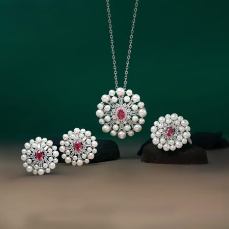 Three pearl-and-diamond pendant necklaces hanging on chains against a dark green background.