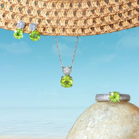Green gemstone jewelry set (necklace and matching earrings) displayed on a rock with a woven hat and blue sky background.
