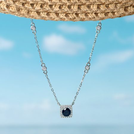 Silver necklace with a dark blue gem pendant, suspended against a bright blue sky.