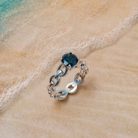 Silver bracelet with a dark blue gemstone resting on wet sand by the ocean.