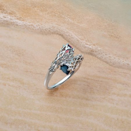 Silver bracelet with a blue gemstone rests on wet beach sand with gentle shoreline foam nearby.