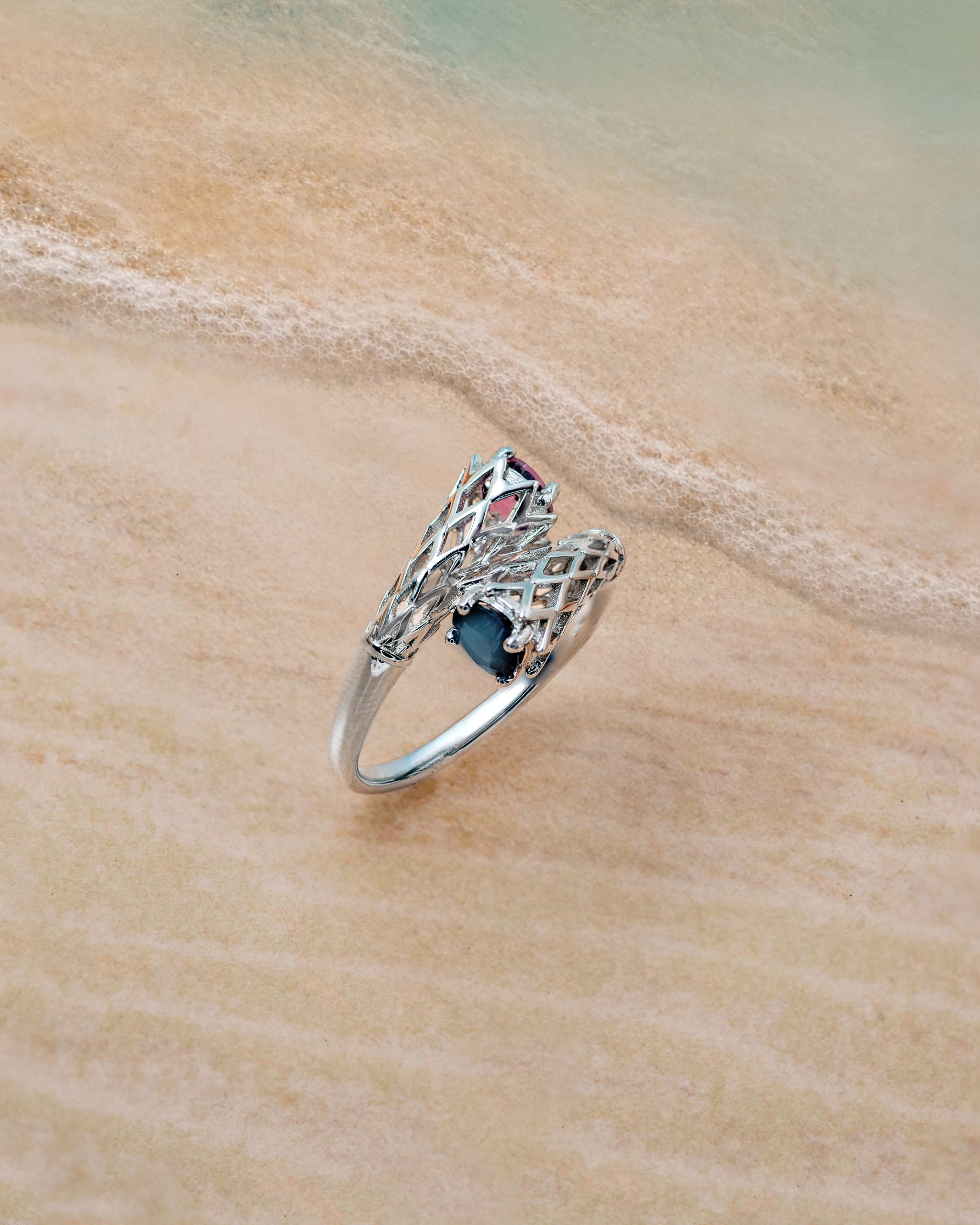 Ring 4 dual stone other Silver bracelet with a blue gemstone rests on wet beach sand with gentle shoreline foam nearby.